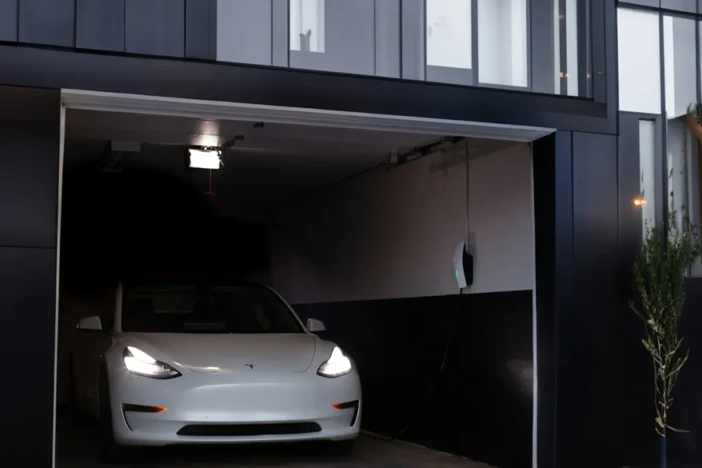 White Tesla parked in a modern residential garage with a wall-mounted home EV charger